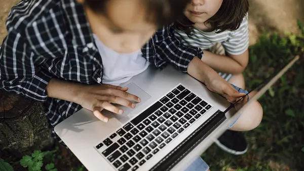 Kids working together on a laptop outside on a cool day in a park setting