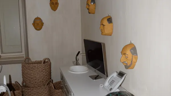 EFTA00001858 - White dresser with a computer monitor phone and turtle figurine sits in a room with several yellow masks on the wall