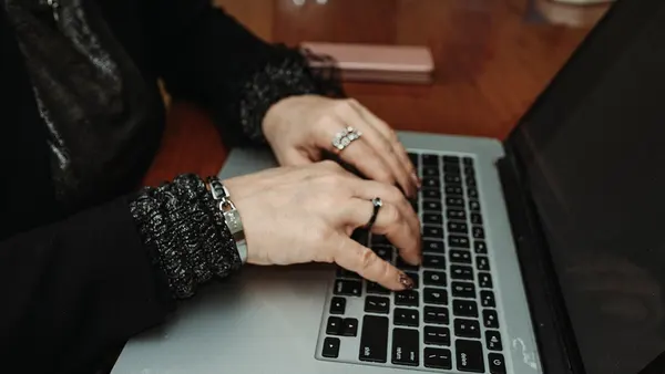 Hands typing on a laptop at a wooden table during a casual indoor setting with a relaxed atmosphere