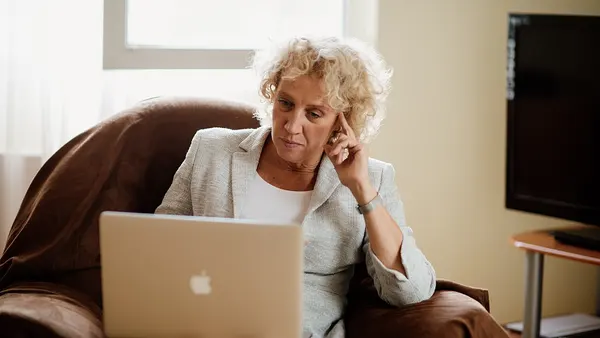 Lonely woman with curly hair sitting in an armchair and working on a laptop at home. (51536554568)