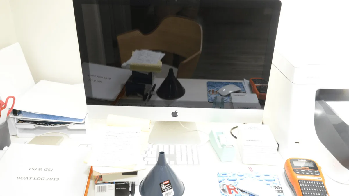 EFTA00002168 - Cluttered desk with a computer monitor printer keyboard and various office supplies including a funnel and a label maker