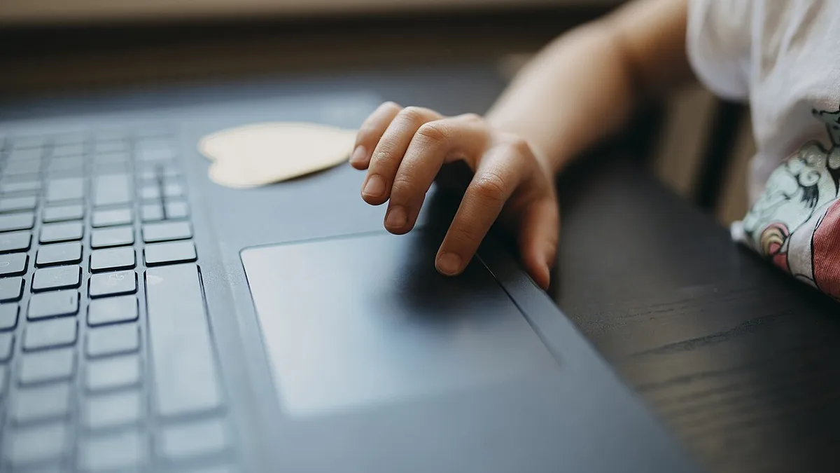 Child interacting with a laptop touchpad while sitting at a table