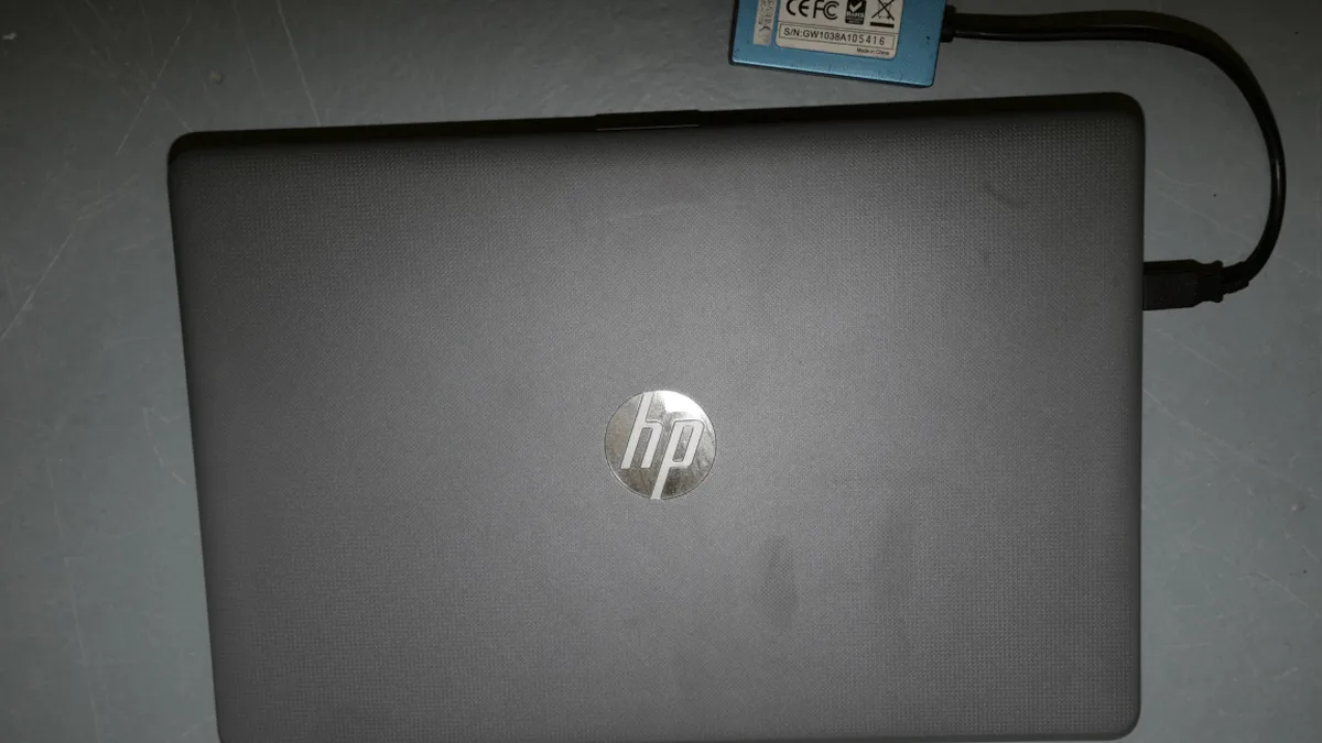 EFTA00002460 - Closed black HP laptop with power adapter connected resting on a scratched gray surface