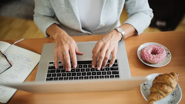 Woman typing on the laptop. One tray with a donut and one tray with a croissant next to her - 51524764031